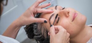 eyebrow specialist holding eyebrow brush over a woman's eyebrow