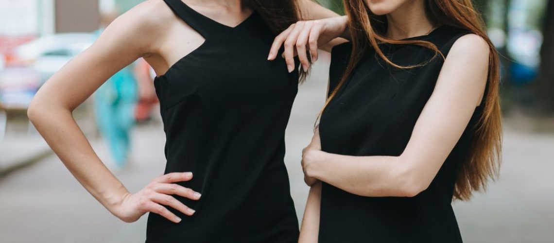 Two women with long hair wearing black dresses