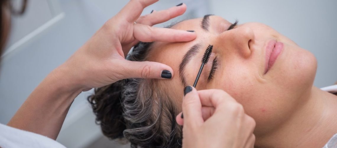 eyebrow specialist holding eyebrow brush over a woman's eyebrow