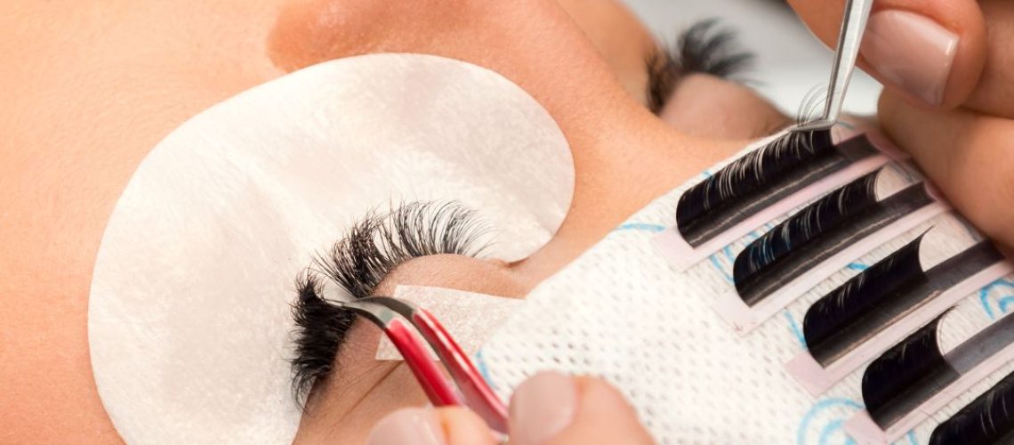 Hands holding tweezers adjusting eyelash extensions